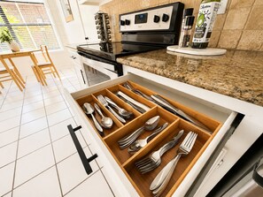 A kitchen with a drawer organizer containing utensils, a stove, and a bottle of organic avocado oil.