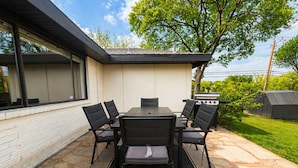 An outdoor patio with a table and chairs, a grill, and a brick wall. - House In The Center Of The DFW Metroplex (Bedford)