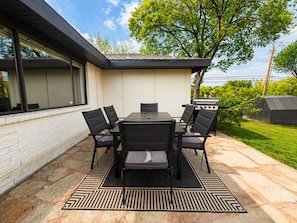 An outdoor patio with a table and chairs, a grill, and a brick wall. - House In The Center Of The DFW Metroplex (Bedford)