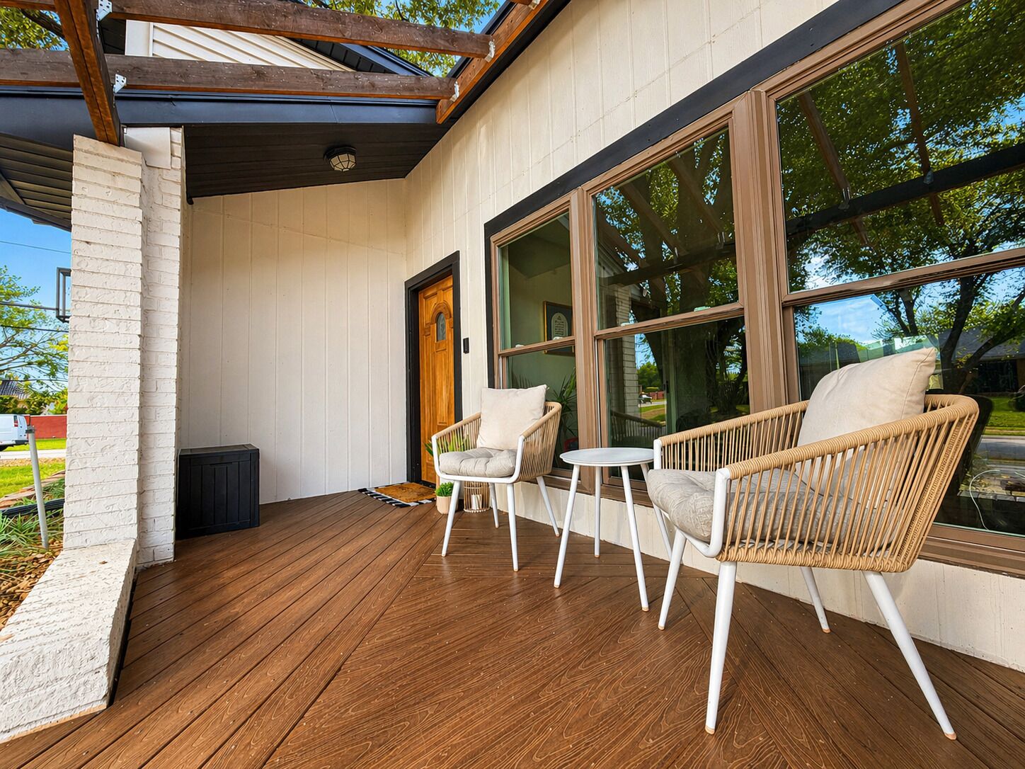 A covered porch with wooden flooring, two wicker chairs, a small table, and a door leading to the interior.
