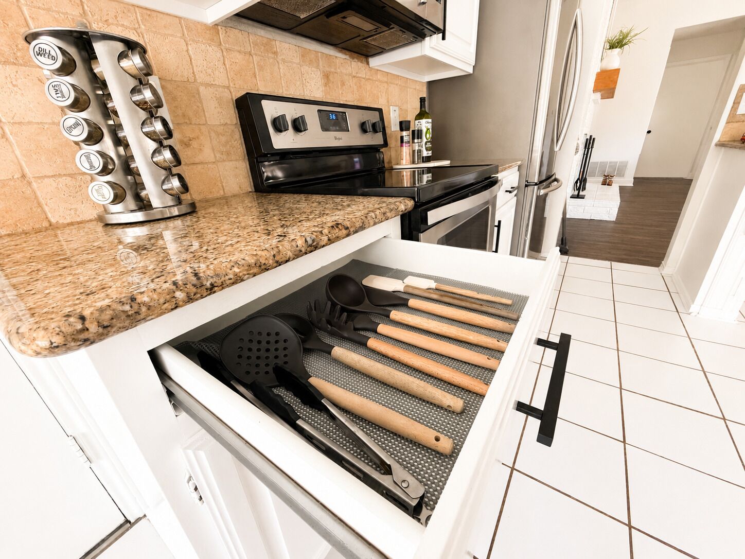 A kitchen with a granite countertop, a built-in oven, and a drawer with cooking utensils.