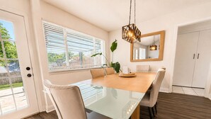 A dining area with a glass-top table, beige chairs, a wooden floor, and a hanging light fixture. - House In The Center Of The DFW Metroplex (Bedford)