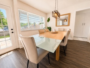 A dining area with a glass-top table, beige chairs, a wooden floor, and a hanging light fixture. - House In The Center Of The DFW Metroplex (Bedford)