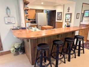 Eine Küche mit Holzschränken, einer Mikrowelle, einem Kühlschrank, einer Holzbar mit Barhocker und einem Blumentopf.