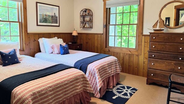 A room with two beds, a dresser, a mirror, and a window with a view. - Island Nights Classic Beach Cottage | Private Association Beach Access (South Haven)