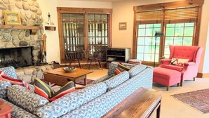 A living room with a stone fireplace, a blue patterned sofa, a wooden coffee table, and a red armchair. - Island Nights Classic Beach Cottage | Private Association Beach Access (South Haven)