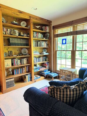 Ein gemütliches Wohnzimmer mit einem großen Bücherregal, gefüllt mit Büchern und Dekoration, einem blauen Sofa mit karierten Kissen und einem kleinen Tisch.