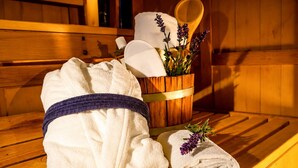 Un banco de madera con una toalla blanca, una toalla enrollada y un cubo de madera que contiene una toalla blanca y flores de lavanda.