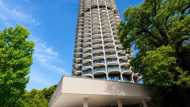 Un edificio alto con varios balcones, rodeado de árboles.