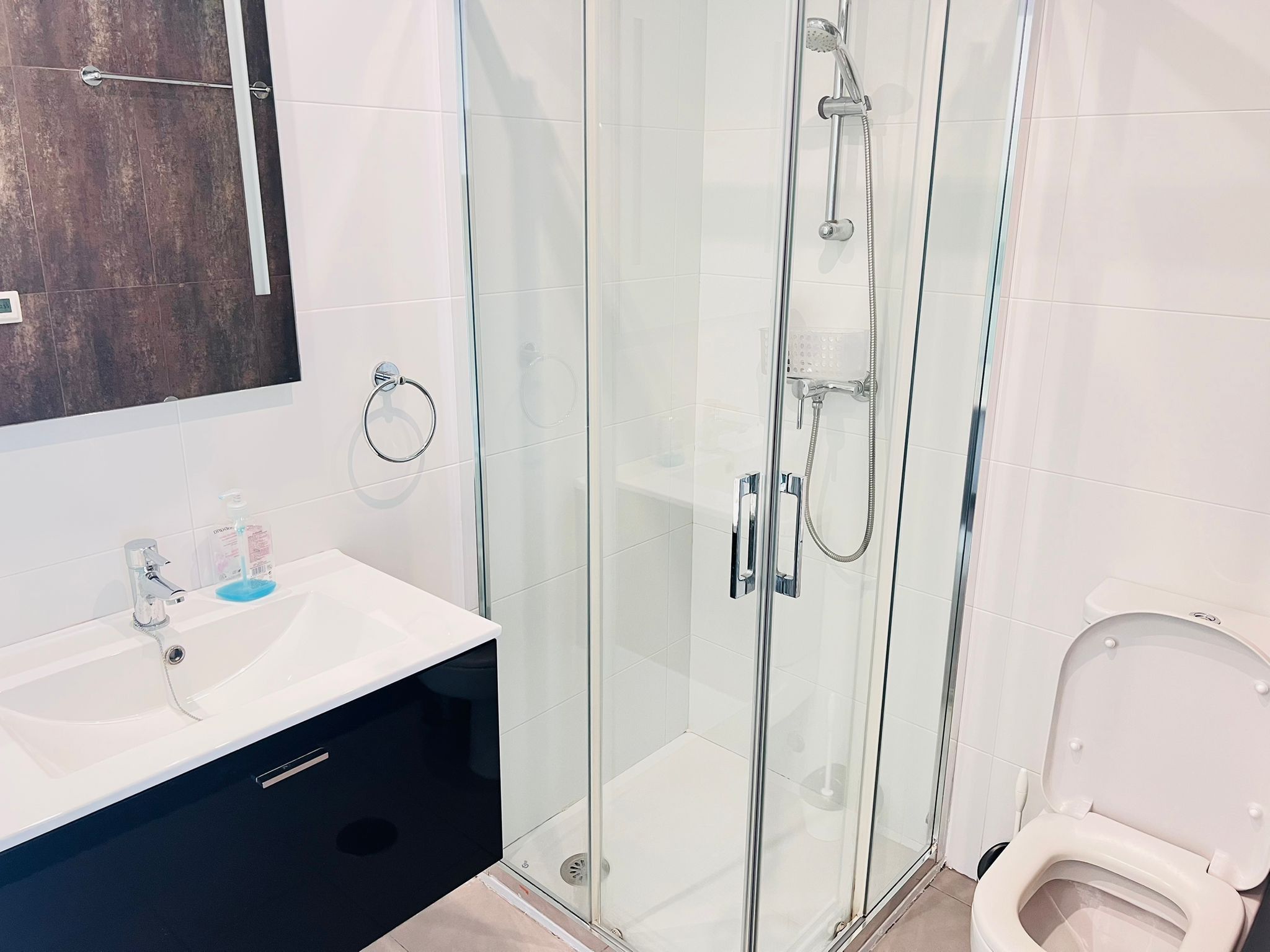 A modern bathroom with a glass-enclosed shower, a white sink with a black cabinet, and a toilet.
