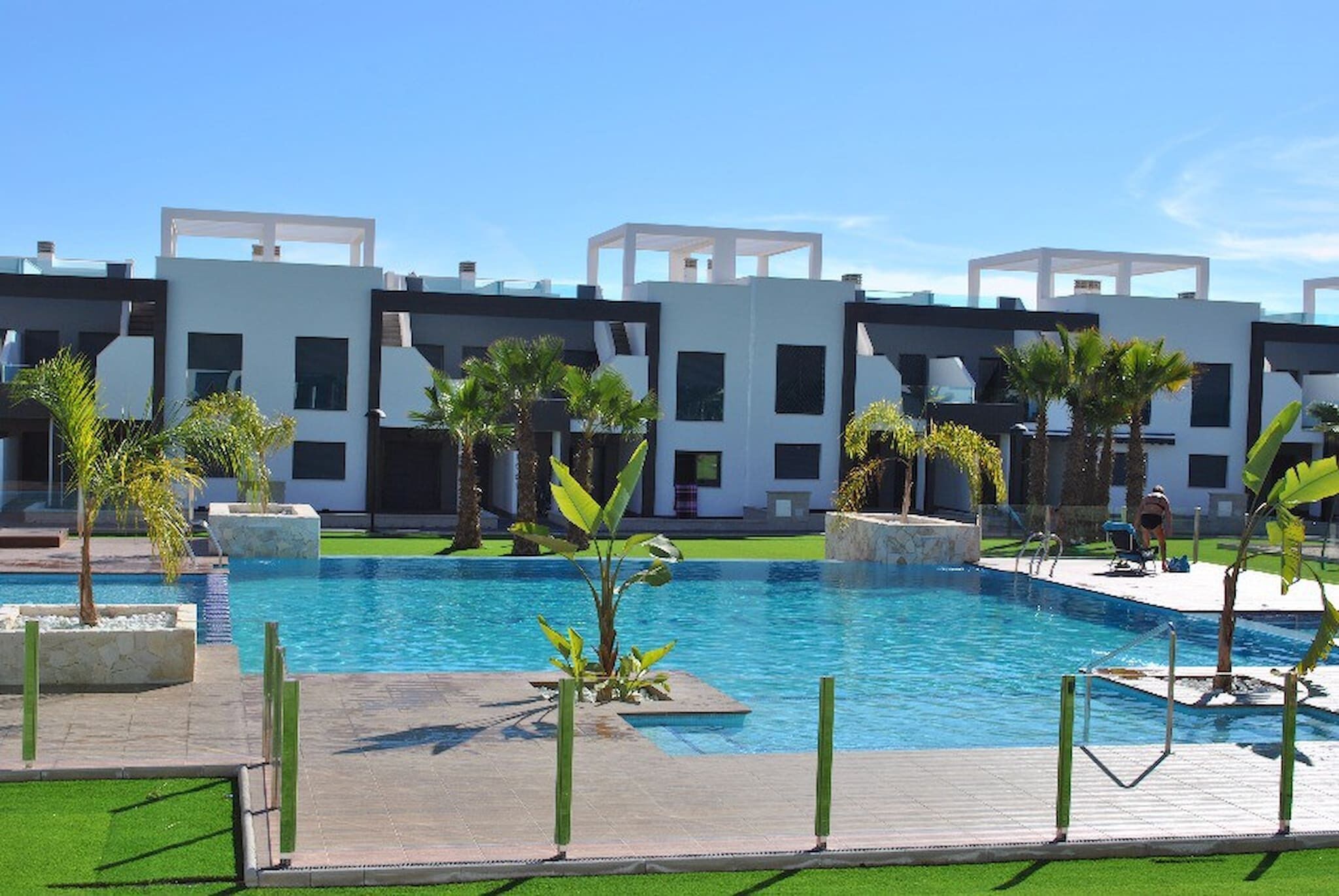 Un hôtel moderne doté d’une piscine, de palmiers et surplombant un ciel d’un bleu limpide.