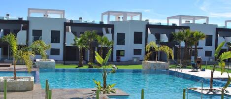 Un hôtel moderne doté d’une piscine, de palmiers et surplombant un ciel d’un bleu limpide.