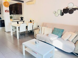 A modern living room with a sofa, a coffee table, and a dining area with chairs and a table. - Penthouse Oasis Beach IV La Zenia (Orihuela)