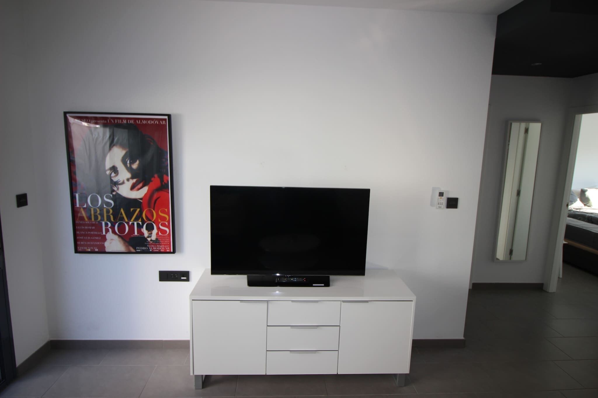 Un salon moderne avec un téléviseur à écran plat posé sur un meuble blanc, une affiche accrochée au mur et une porte donnant sur une autre pièce.