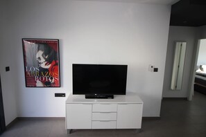 A modern living room with a flat-screen TV on a white cabinet, a poster on the wall, and a door leading to another room. - Penthouse Oasis Beach IV La Zenia (Orihuela)