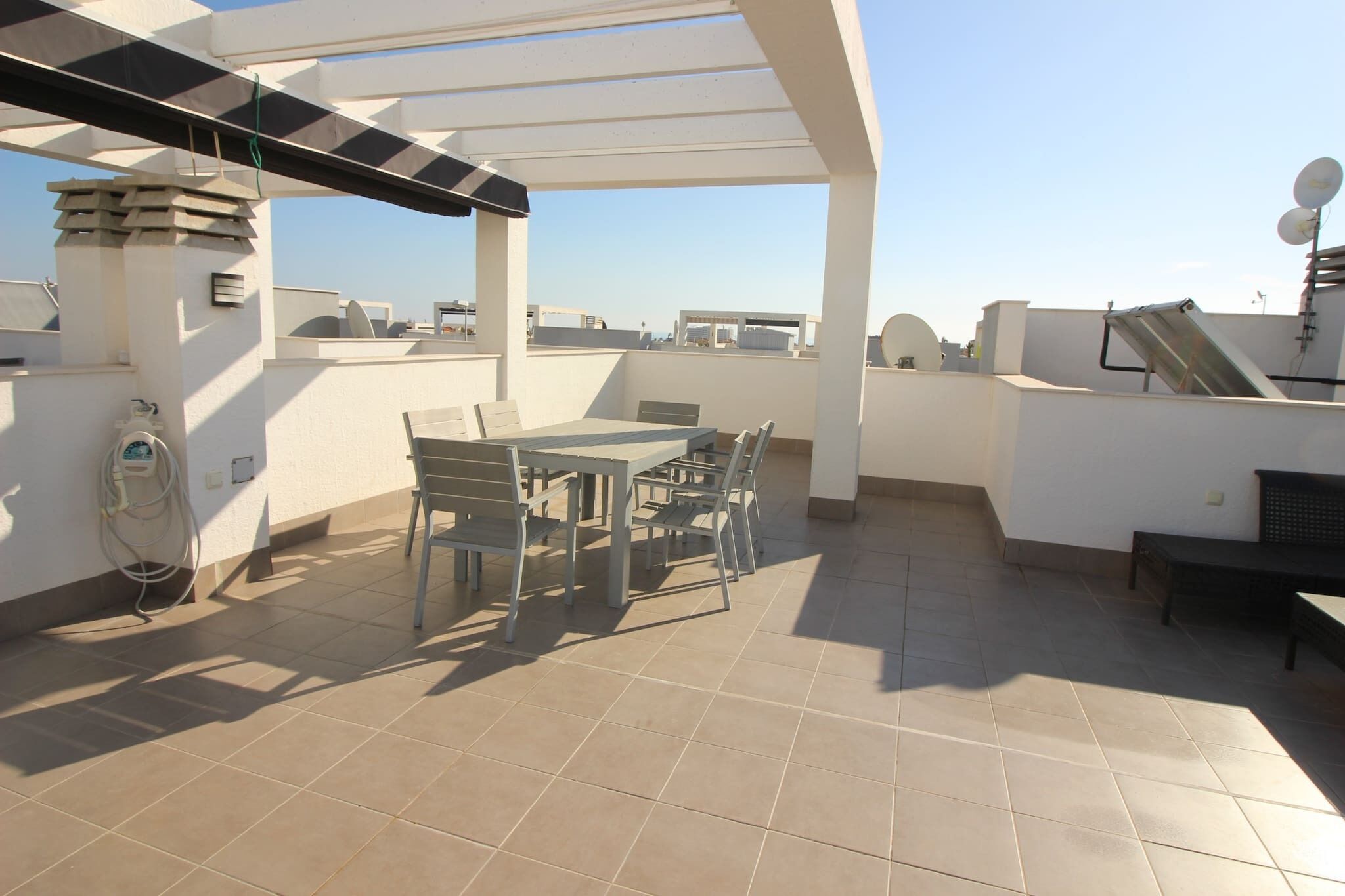Un patio en la azotea con mesa y sillas, un pérgola y vistas de la ciudad.