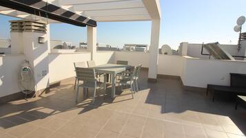 Un patio en la azotea con mesa y sillas, un pérgola y vistas de la ciudad.