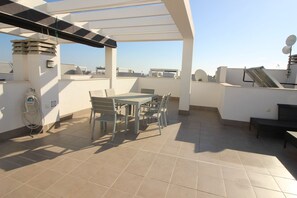 Un patio en la azotea con mesa y sillas, un pérgola y vistas de la ciudad.