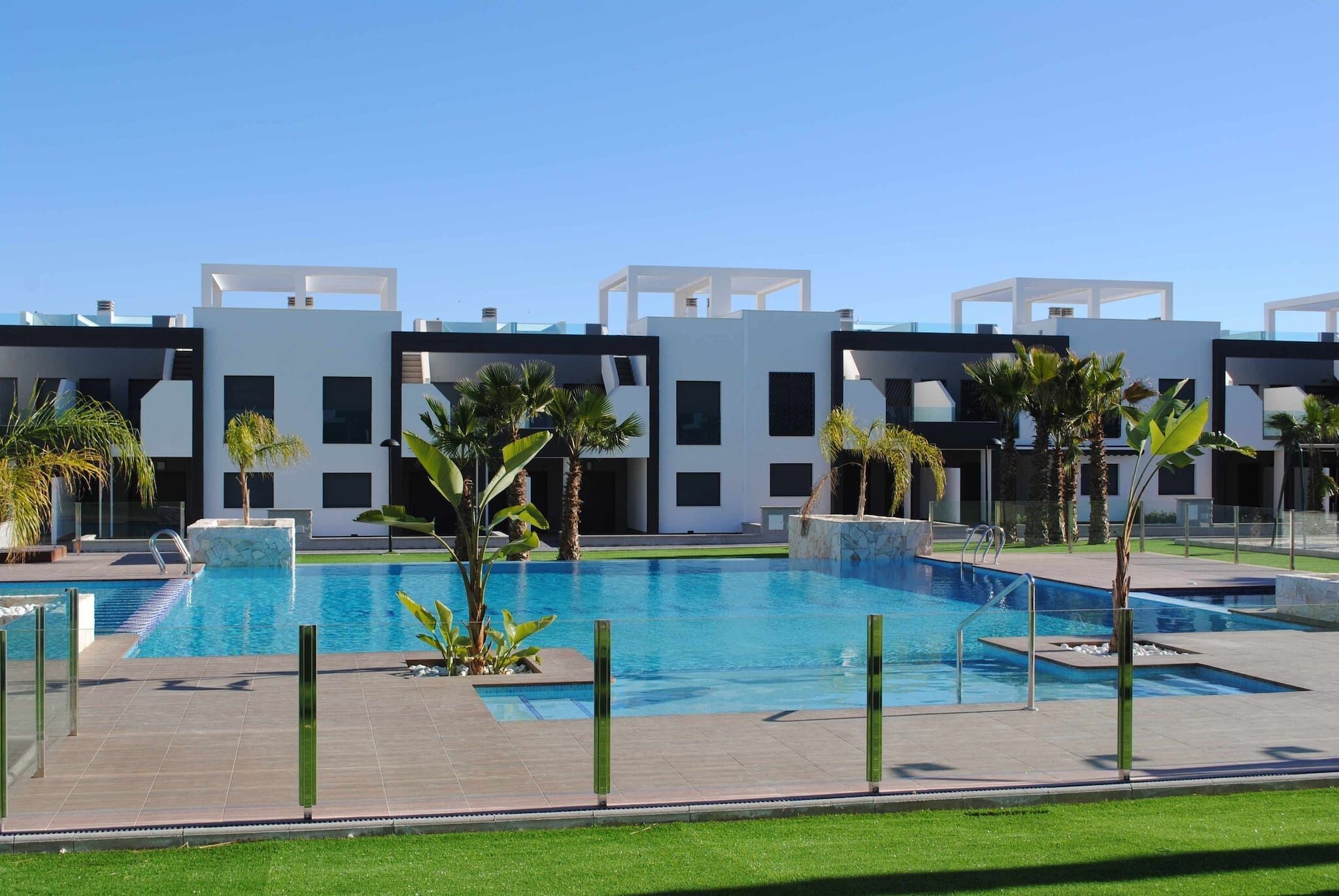 Un hôtel moderne doté d’une piscine, de palmiers et surplombant un ciel d’un bleu éclatant.