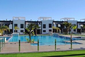 A modern hotel with a swimming pool, palm trees, and a clear blue sky. - Penthouse Oasis Beach IV La Zenia (Orihuela)