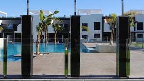 A modern pool area with clear blue water, surrounded by glass pillars and palm trees. - Penthouse Oasis Beach IV La Zenia (Orihuela)