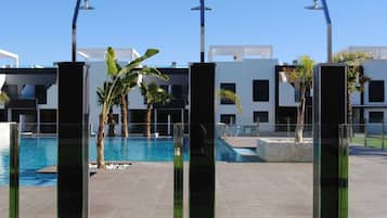 A modern pool area with clear blue water, surrounded by glass pillars and palm trees.