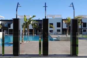 A modern pool area with clear blue water, surrounded by glass pillars and palm trees. - Penthouse Oasis Beach IV La Zenia (Orihuela)