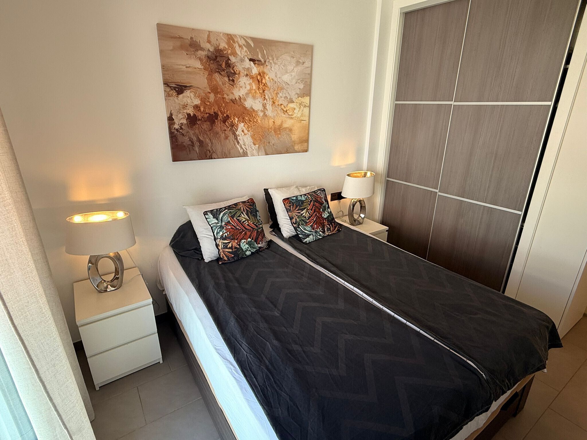 Un dormitorio moderno con cama, dos lámparas de noche, una mesita de noche, un cuadro abstracto grande y un armario.