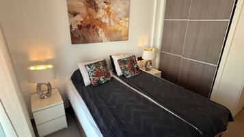 Un dormitorio moderno con cama, dos lámparas de noche, una mesita de noche, un cuadro abstracto grande y un armario.
