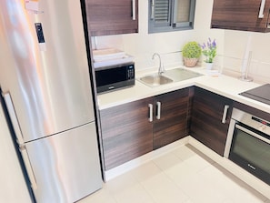 Una cocina moderna con electrodomésticos de acero inoxidable, armarios de madera oscura, un microondas y un lavamanos.