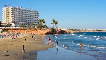 Un hotel de varios pisos, una playa en primer plano y palmeras.