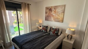 A bedroom with a bed, two bedside lamps, a nightstand, a window with curtains, and a painting on the wall. - Penthouse Oasis Beach IV La Zenia (Orihuela)