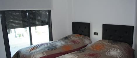 A bedroom with a bed, a window with blinds, and a wall-mounted light switch.