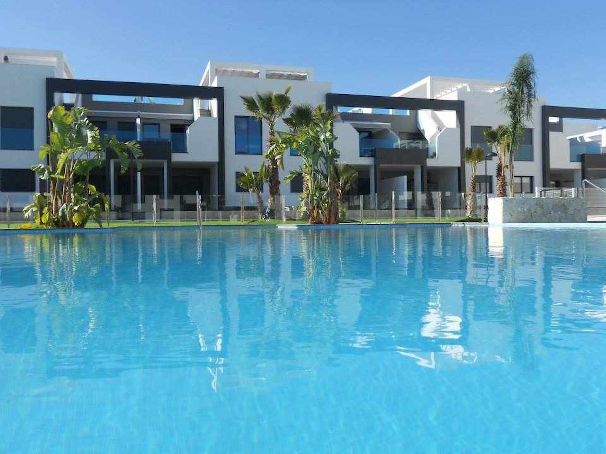 Un hôtel moderne doté d’une piscine, de palmiers et surplombant un ciel d’un bleu limpide.
