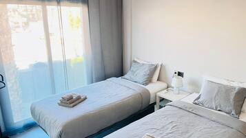 Una habitación de hotel con dos camas individuales, una mesita de noche con lámpara y una ventana con cortinas.