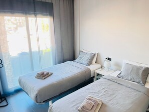 Una habitación de hotel con dos camas individuales, una mesita de noche con lámpara y una ventana con cortinas.