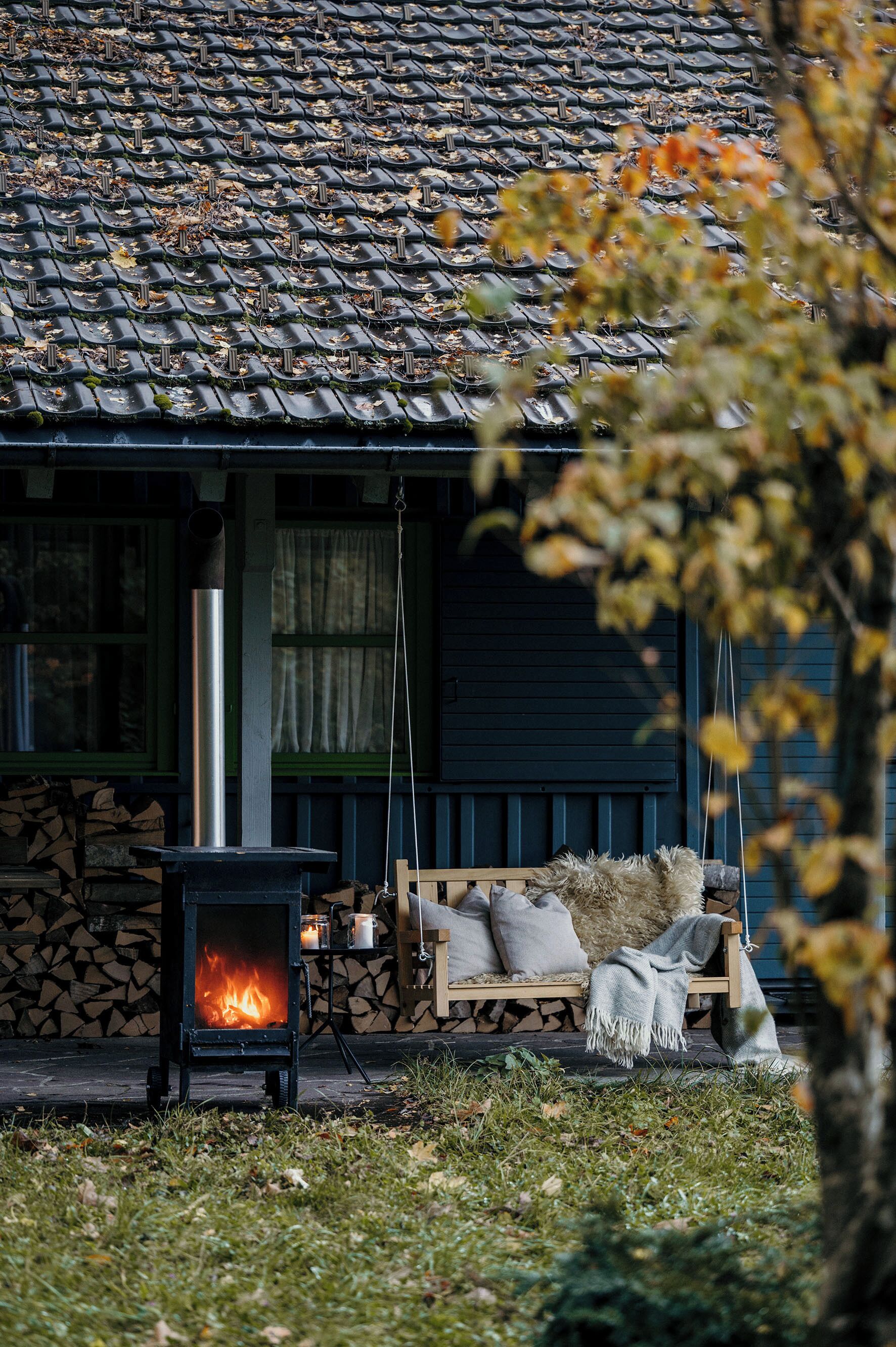 A cozy outdoor seating area with a wood-burning stove, a stone wall, and a swing chair.