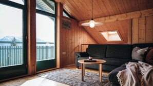 Una habitación acogedora con techo de madera, un ventanal grande, un sofá, una mesita y vistas a la montaña.