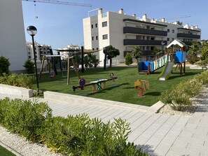 Ein Spielplatz mit Schaukeln, einer Rutsche und einer Kletteranlage.