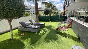 Un patio con césped artificial, sillones de descanso y una pequeña mesa.