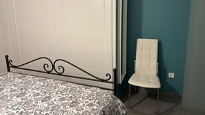 Un dormitorio con una cama, una silla blanca y una pared color verde azulado.