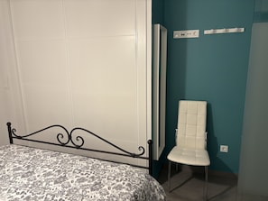 Un dormitorio con una cama, una silla blanca y una pared color verde azulado.
