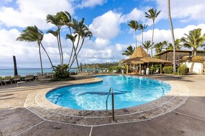 A resort pool with a circular design, surrounded by lounge chairs and palm trees, with a view of the ocean. - Napili Shores D-232 - Upper Level Renovated Studio at Koi Pond, Wi-fi & Split AC (Lahaina)