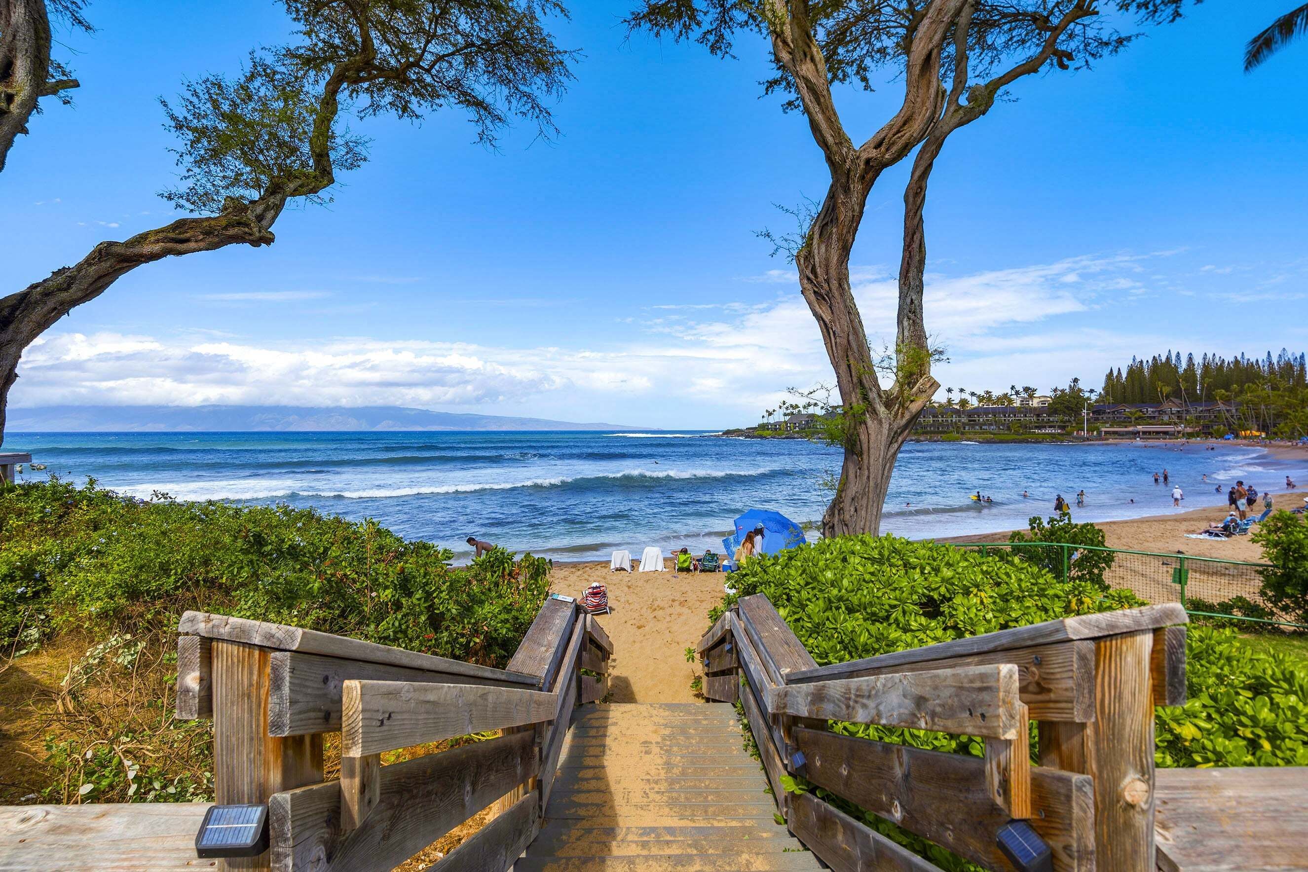 A wooden staircase leading to a beach with ocean views, a sandy path, and a clear sky.