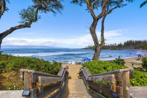 Una escalera de madera que lleva a una playa con vistas al océano, arena y algunas sombrillas.