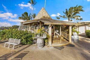 A tiki hut with a conical roof, surrounded by palm trees and a bench. - Napili Shores D-232 - Upper Level Renovated Studio at Koi Pond, Wi-fi & Split AC (Lahaina)