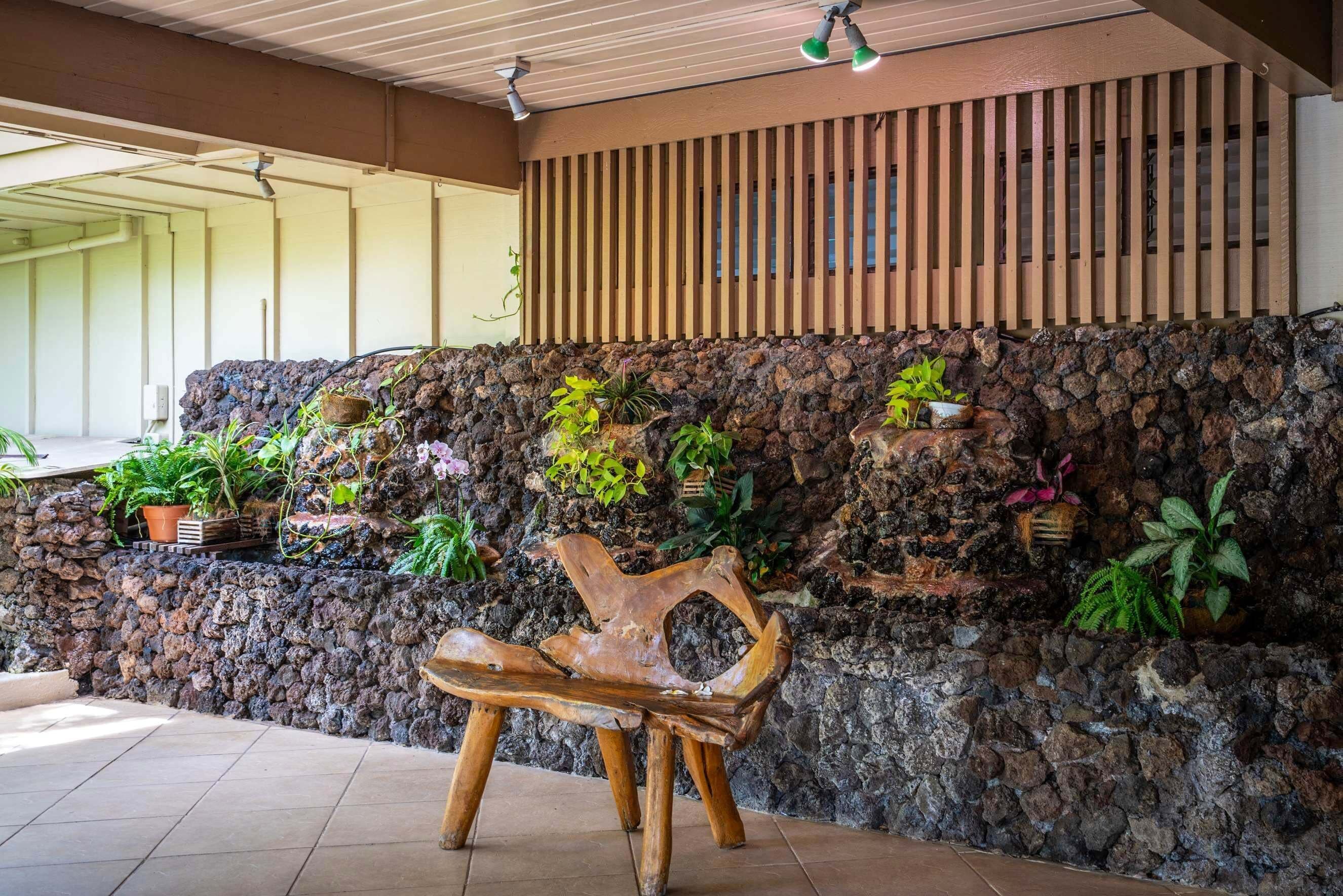 A stone wall with various potted plants and a wooden bench in a shaded outdoor area.