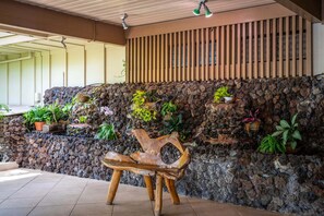 Un mur de pierre agrémenté de différents pots de plantes et d’un banc en bois, le tout situé dans un espace extérieur ombragé.