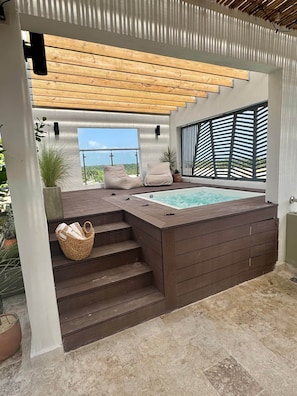 Ein moderner Außenbereich mit Whirlpool, der von Holzwegen und Kübelpflanzen gesäumt wird, mit Blick auf den Himmel.