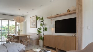 A modern living room with a sofa, a round coffee table with books, a dining area with a table and chairs, and a TV mounted on the wall. - Altamar — Rooftop Penthouse, Private Jacuzzi, Walk to Encuentro Beach, Sleeps 8 (playa encuentro- cabarete)